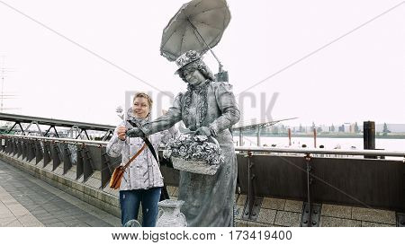 Hamburg, Germany - October, 10, 2016: Living statue street performer in Hamburg port poses with tourist to take a photo. Living statues acting is a popular way to entertain passersby and tourists.