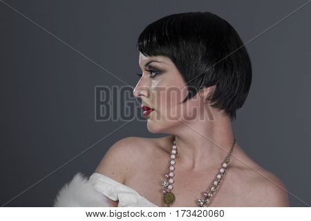 Flapper, 1920s style brunette dancer with short hair and jewelry. She is wearing a white hair shawl