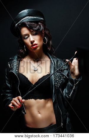 portrait of young woman wearing leather jacket and hat holding whin in her arms posing next to color background