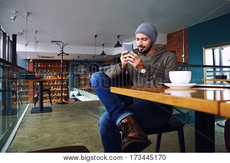 Young fashion hipster drinking espresso coffee in city cafe during lunch time and working on tablet computer