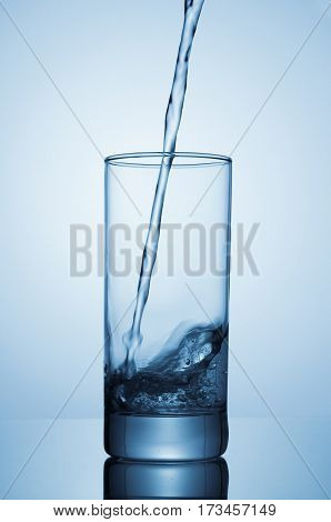 Sparkling water pouring into glass on blue background