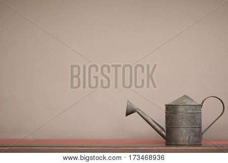 close up vintage style watering can on shelf with brown wall background