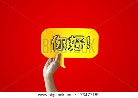 Human Hands Holding 'Nihao' Yellow Speech Bubble Over Red Background - Chinese language learning concept