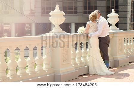 Happy bride and groom are the backs of the white marble railing in the sunshine