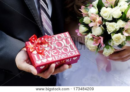 The red box with love in the hands of the bride and bouquet in hands of bride closeup