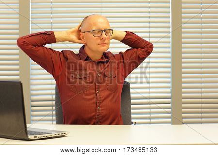 middle age balding man relaxing neck - stretching arms - short break for exercise on chair in office