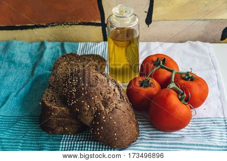 Olive oil tomato and slides of brown bread on tablecloth