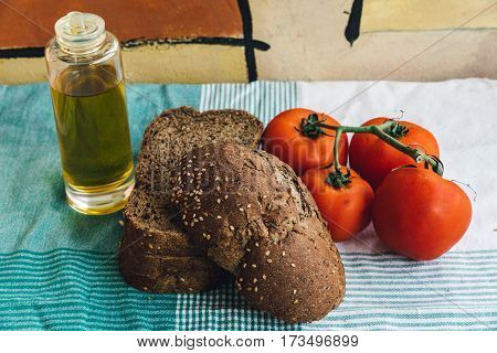 Olive oil tomato and slides of brown bread on tablecloth