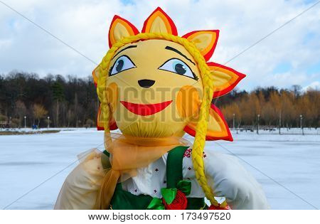 Shrovetide doll in green sarafan and white embroidered shirt with face-sun on background of spring landscape