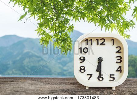 Closeup white clock for decorate show half past six or 6:30 a.m. on blurred mountain view background
