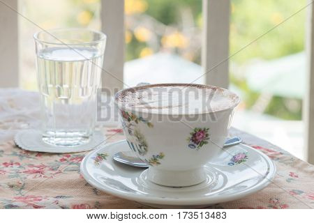 Cafe art latte coffee in the vintage cup on the tabel with a glass of water on the table