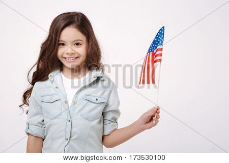 Proud to be the citizen of this country. Joyful delighted cheerful girl holding the American flag while expressing positivity and standing isolated in white background