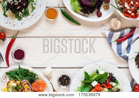 Fresh vegetable salads frame flat lay. Top view on white wooden table with free space for text between side dish buffet. Vegetarian cuisine, menu concept