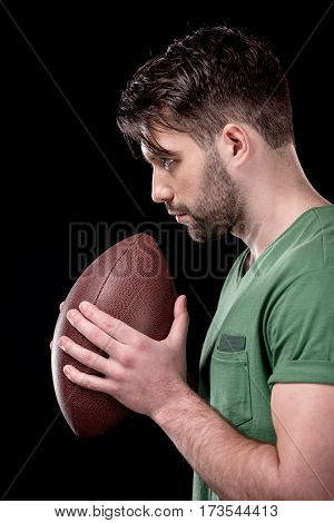 side view of concentrated man holding rugby ball on black