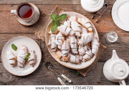Rugelach with jam filling on plate with tea on wooden background, top view with copy space