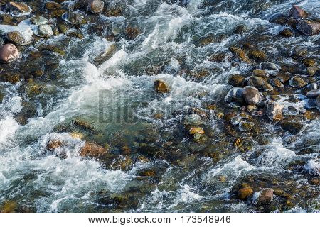 Raging water breaker among icy rocks with frazil of mountain river in winter