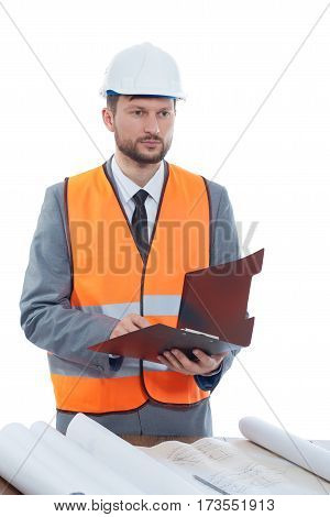 Experienced engineer. Male construction foreman in a safety vest and a helmet looking away thoughtfully making notes in his clipboard businesspeople building construction industry development concept