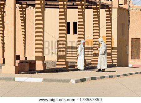 Merzouga Morocco - Jan 6 2017: Two Moroccan men in white djellaba talk on the street in Merzouga village