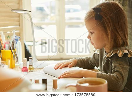 Little girl in nail salon receiving manicure by beautician. Little girl getting manicure at beauty salon