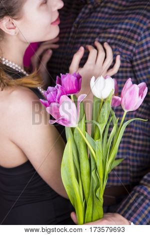 Beautiful young romantic couple with tender bouquet of pink and white tulips on bright crimson background