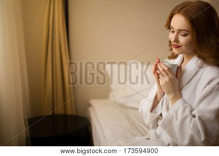 Red-haired girl with a cup of coffee in bed