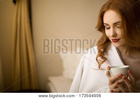 Red-haired girl with a cup of coffee in bed