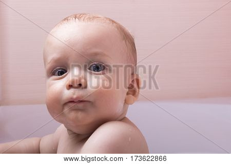 Serious 9-month baby is taking a bath and looking to the camera