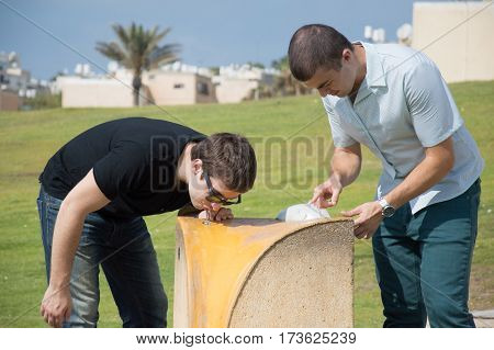 Two men drinking water from water fountain cooler in city park.