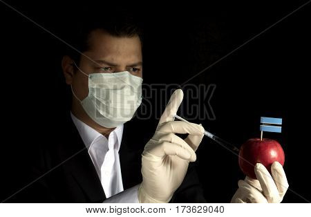 Young Businessman Injecting Chemicals Into An Apple With Botswanan Flag On Black Background