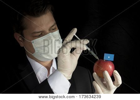 Young Businessman Injecting Chemicals Into An Apple With Somalian Flag On Black Background