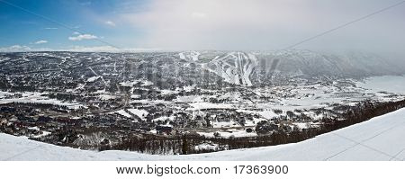 Panoramatický pohled na malé město v údolí s zimní horské svahy a lyžařské trasy