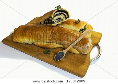 Poppy roll baked at home with sprigs of mint on a wooden board with a wooden spoon filled with grains of poppy. Isolated on white background.