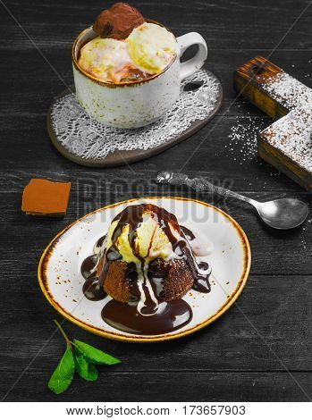 Chocolate lava cake (Molten) with ice cream on plate. Balls of ice cream in cup. Chocolate lava cake (Molten) with mint on board. Pieces of chocolate. Dark black wooden background.