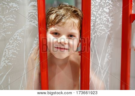 Happy little kid boy in the shower cabin wet and smiling. Adorable child with blond hairs taking bath and having fun.
