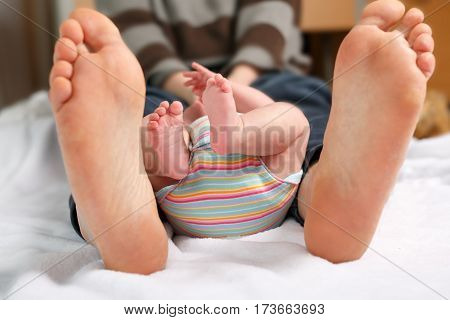 Closeup of huge feet of father and little newborn baby. Big feet of adult and tiny legs of child. Happy parenthood, carefree childhood, family, love, tenderness.