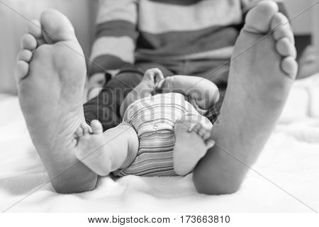 Closeup of huge feet of father and little newborn baby. Big feet of adult and tiny legs of child. Happy parenthood, carefree childhood, family, love, tenderness. In black-and-white, monochrome