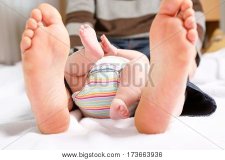 Closeup of huge feet of father and little newborn baby. Big feet of adult and tiny legs of child. Happy parenthood, carefree childhood, family, love, tenderness.