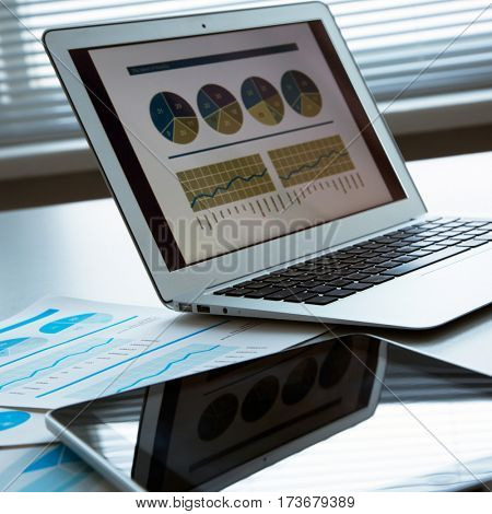 The workplace of business people. Laptop, raphs, charts, business table.