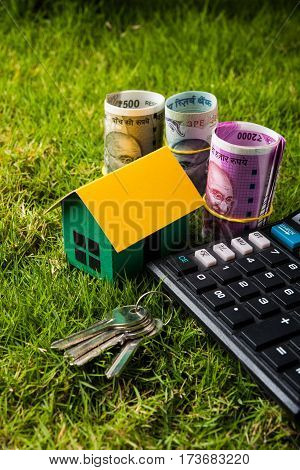 indian currency notes of rupees 100, 500 and 2000 in roll or stack with small home model, keys, toy car and calculator with blank board over green grass - home buying and finance concept in India