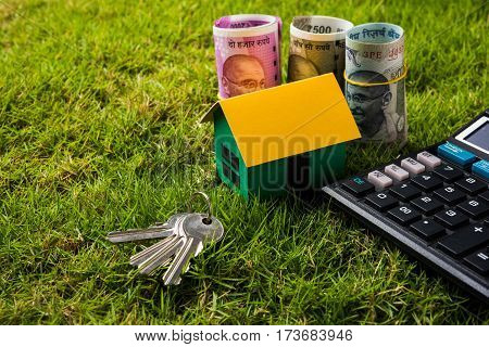 indian currency notes of rupees 100, 500 and 2000 in roll or stack with small home model, keys, toy car and calculator with blank board over green grass - home buying and finance concept in India