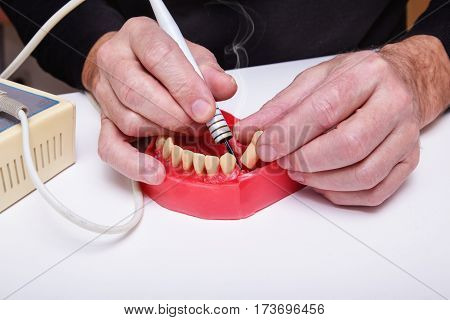 Close up of men's hands working with electric waxer on a red wax dental model on a white table