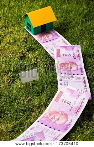 indian new currency notes of rupees 500 or 2000 forming a road to reach model house over green grass  - concept of residential property or home buying in india