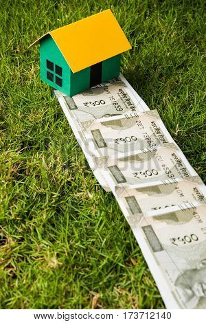 indian new currency notes of rupees 500 or 2000 forming a road to reach model house over green grass  - concept of residential property or home buying in india