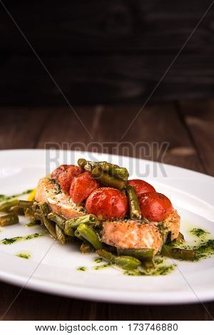 Grilled trout with tomatos leguminous beans and lemon on white plate. Top view