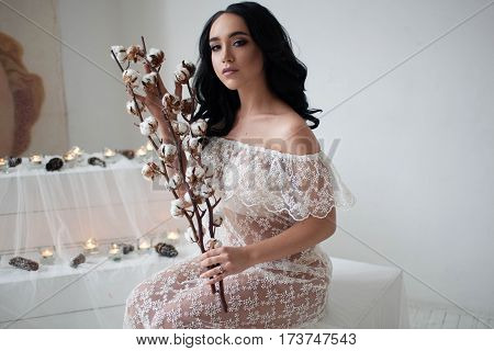 Gorgeous sexy dark-haired young woman with provocative make-up and hairstyle of hair in a transparent white negligee holding cotton thread