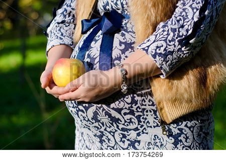 pregnant woman in blue dress holds a round yellow apple
