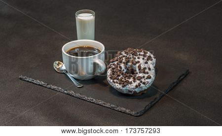 right view on an aromatic black coffee in a white cup with coconut liqueur in a glass with two oreo doughnut on a black stone plate the party set