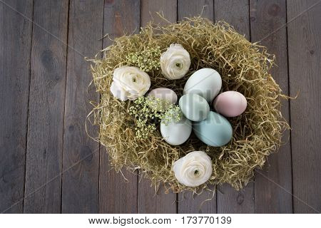 Close up of pastel colored easter eggs in a nest of straw on a dark shabby wooden table