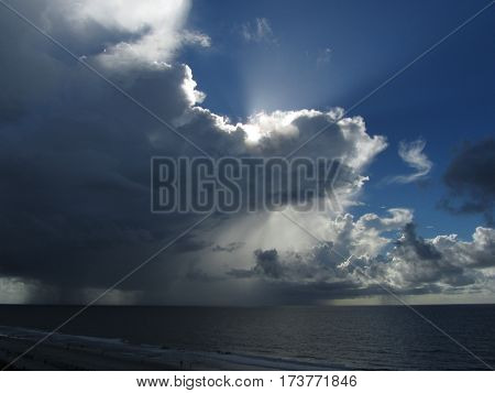 sunlight streaming from behind cumulus clouds and rain squall over the Atlantic ocean