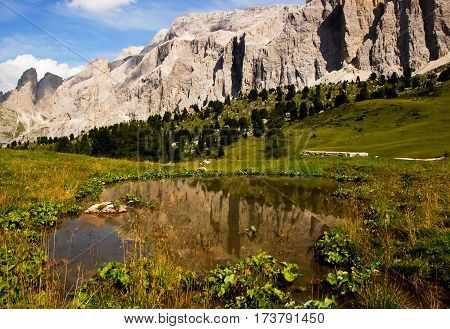 small pond under dolomites mountains in italy on a blue sky background